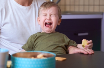 A small child is crying with a parent holding him in front of a blue bowl on a table